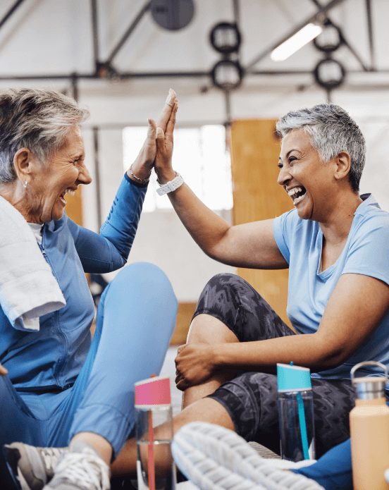 Two senior women smile and high five during workout