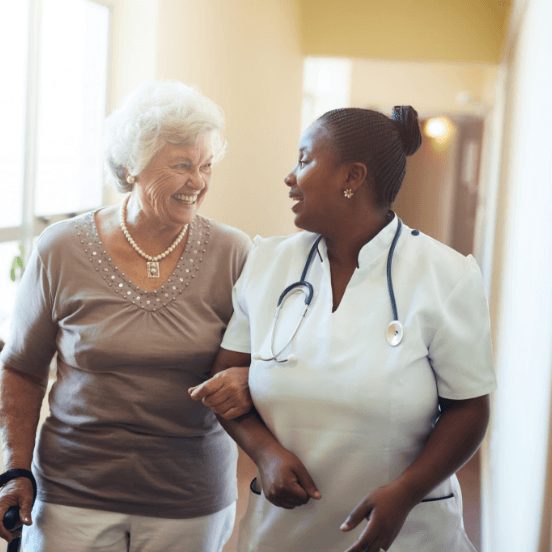 Senior woman and nurse walk through a hallway together