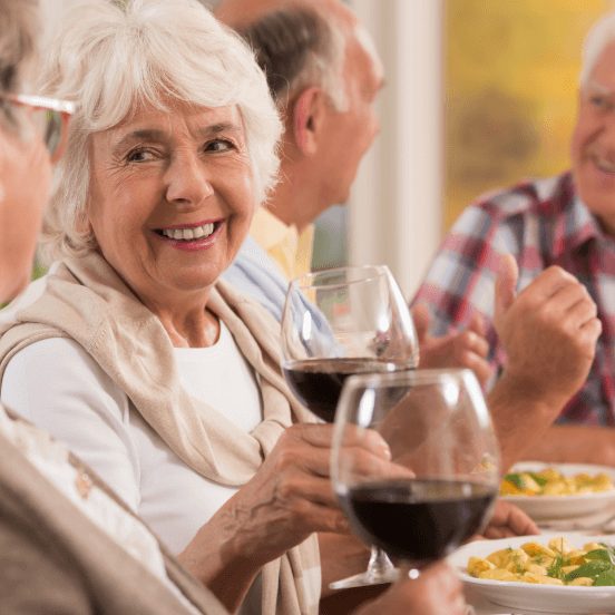 Seniors around dinner table talk and drink wine