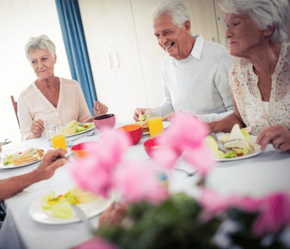 Senior friends sit around dining table with pink flowers