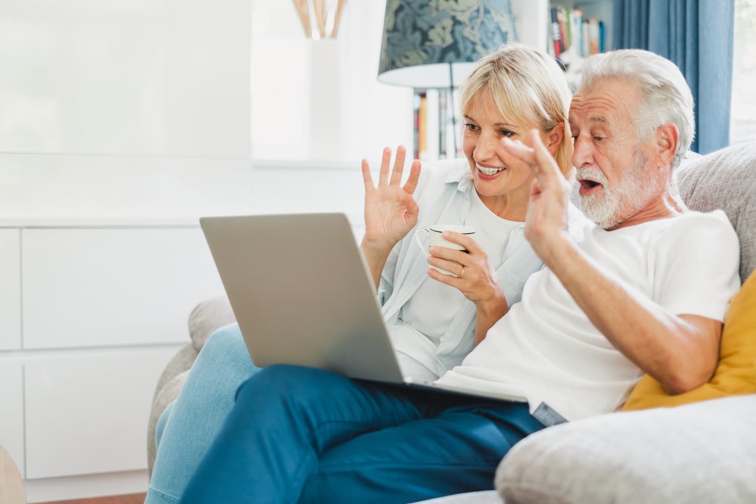 Senior couple smiling and waving to computer